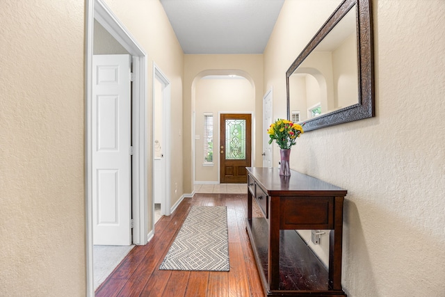 doorway featuring arched walkways, hardwood / wood-style floors, a textured wall, and baseboards