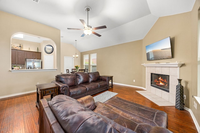 living area featuring vaulted ceiling, hardwood / wood-style flooring, a tile fireplace, baseboards, and ceiling fan
