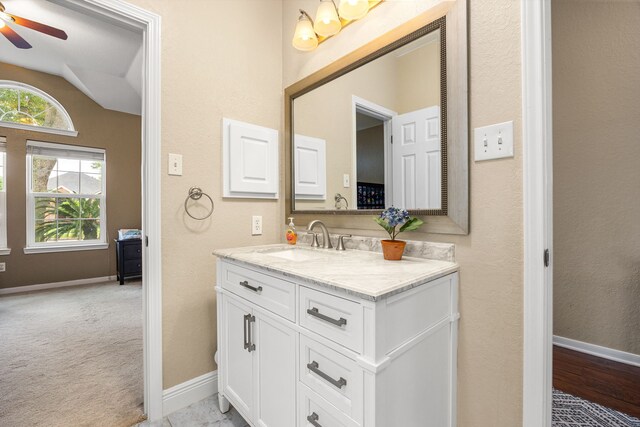bathroom featuring vanity, ceiling fan, baseboards, and vaulted ceiling