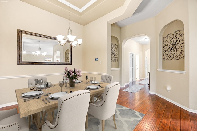 dining room with a chandelier, wood-type flooring, arched walkways, and baseboards
