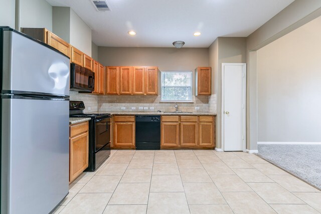 kitchen with black appliances, tasteful backsplash, a sink, light carpet, and light stone counters