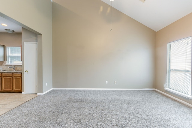 unfurnished room with light colored carpet, lofted ceiling, baseboards, a sink, and a ceiling fan