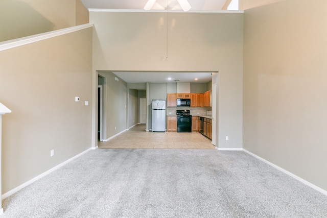 unfurnished living room with light carpet, baseboards, a high ceiling, and a ceiling fan