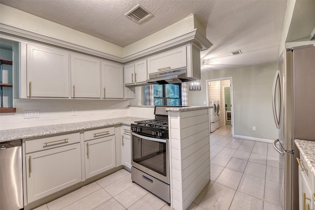 4650 Hickory Downs Dr, Houston, TX 77084 - kitchen with stainless steel appliances, washer and dryer, light tile patterned floors, a textured ceiling, and under cabinet range hood