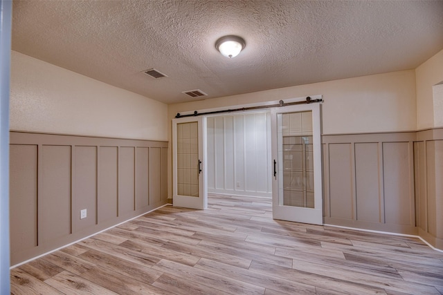4650 Hickory Downs Dr, Houston, TX 77084 - spare room with a decorative wall, a barn door, a wainscoted wall, a textured ceiling, and light wood-style floors