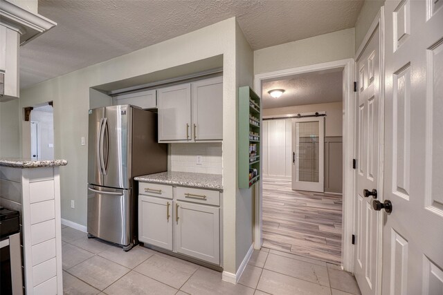 4650 Hickory Downs Dr, Houston, TX 77084 - kitchen with freestanding refrigerator, a textured ceiling, light tile patterned floors, a barn door, and baseboards