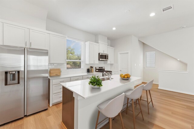 kitchen with appliances with stainless steel finishes, decorative backsplash, light wood-type flooring, a kitchen breakfast bar, and an island with sink