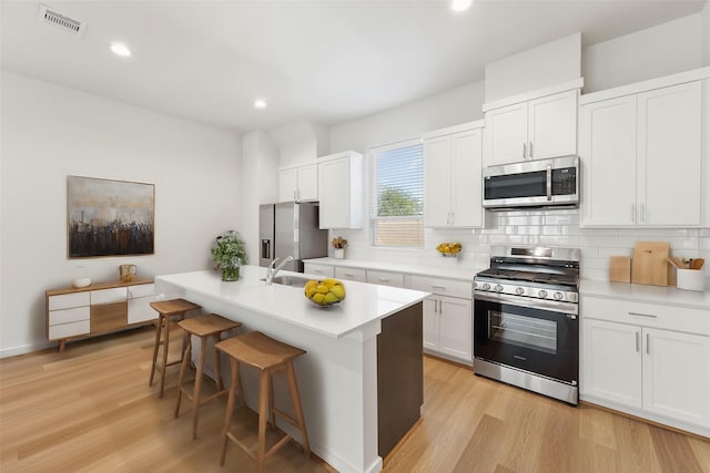kitchen with stainless steel appliances, a sink, backsplash, light wood-style flooring, and recessed lighting