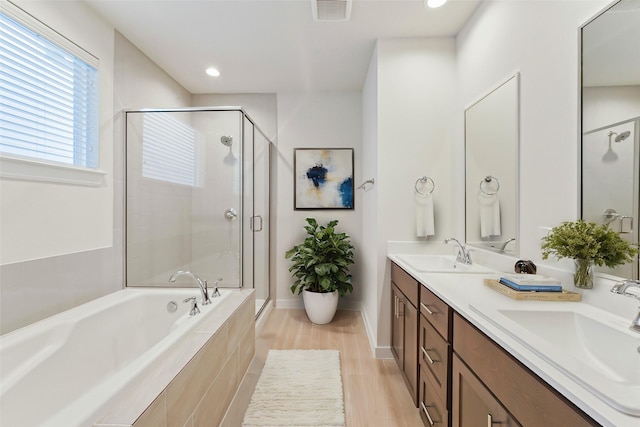 bathroom with a bath, a shower stall, double vanity, recessed lighting, and wood finished floors
