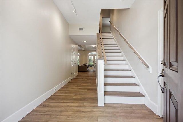 entrance foyer featuring stairs, baseboards, rail lighting, and wood finished floors