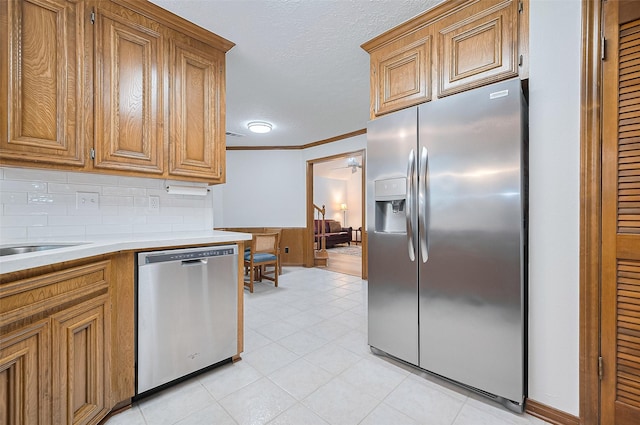 16218 Capri Dr, Jersey Village, TX 77040 - kitchen featuring appliances with stainless steel finishes, brown cabinets, light countertops, light tile patterned floors, and decorative backsplash