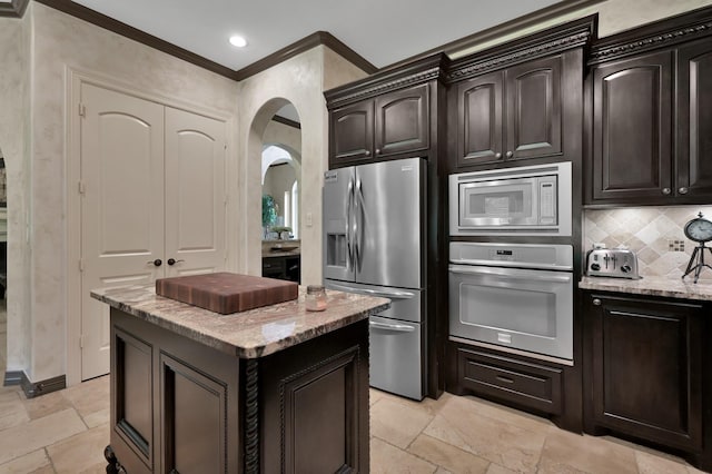 26118 Upper Beacon Pl, Montgomery, TX 77316 - kitchen featuring appliances with stainless steel finishes, stone tile flooring, light stone counters, a center island, and arched walkways