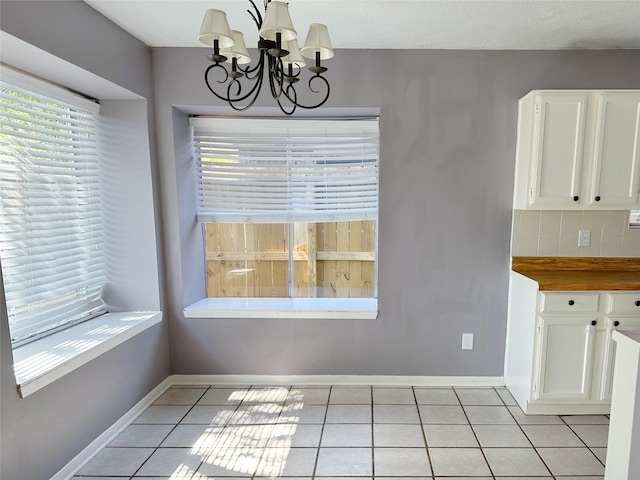 unfurnished dining area with a chandelier, light tile patterned floors, and baseboards