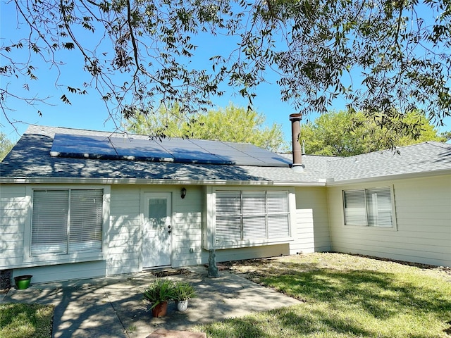 rear view of property featuring solar panels, a patio, a lawn, and a shingled roof