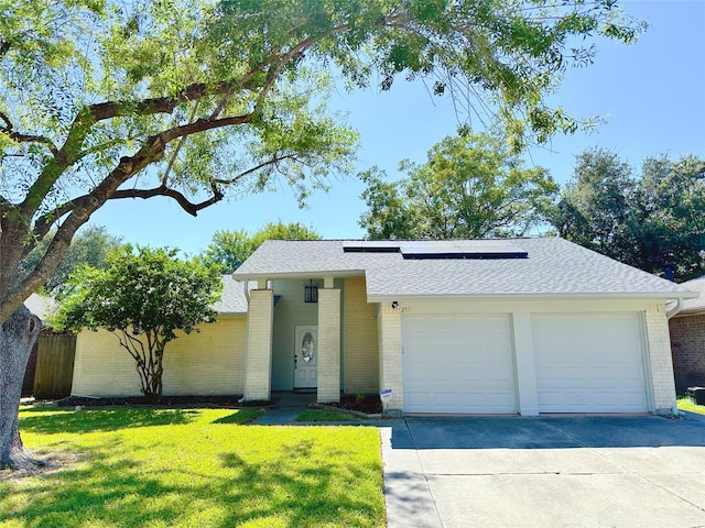 view of front of home with brick siding, an attached garage, roof mounted solar panels, concrete driveway, and a front lawn