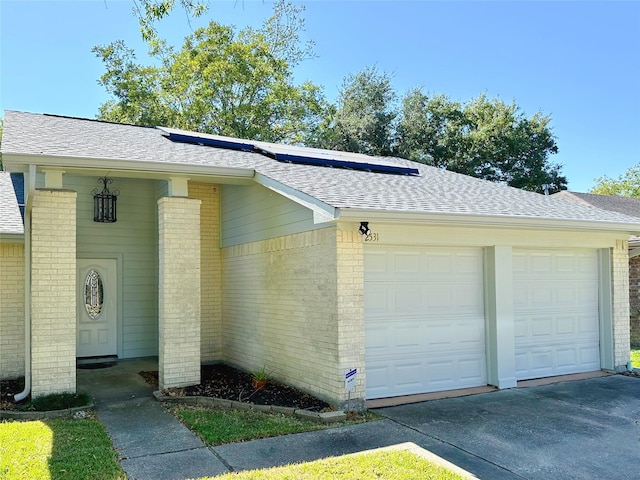 ranch-style home featuring brick siding, roof mounted solar panels, a shingled roof, and a garage