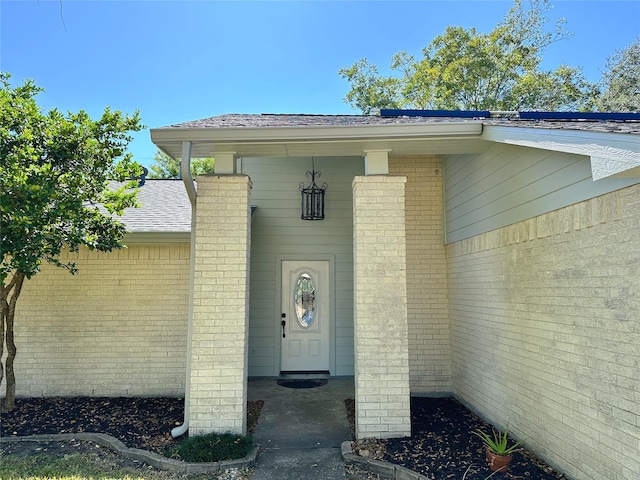 doorway to property with roof with shingles and brick siding
