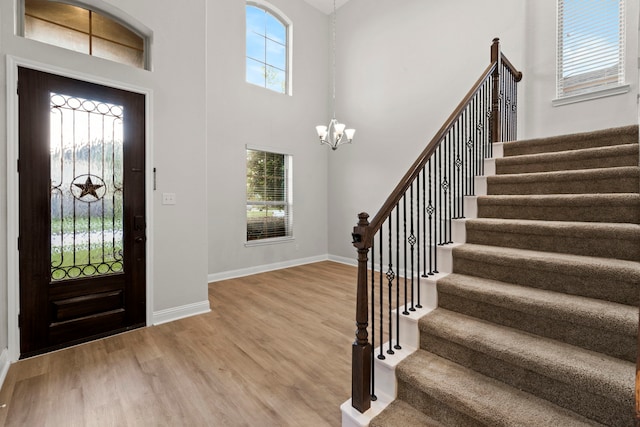 foyer featuring stairway, a chandelier, wood finished floors, baseboards, and a high ceiling