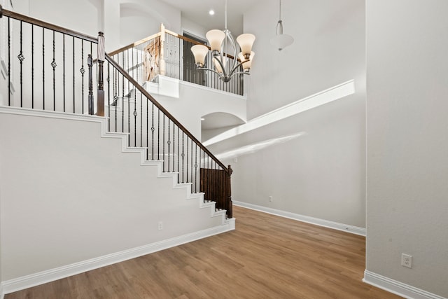 stairway featuring a high ceiling, a chandelier, baseboards, and wood finished floors
