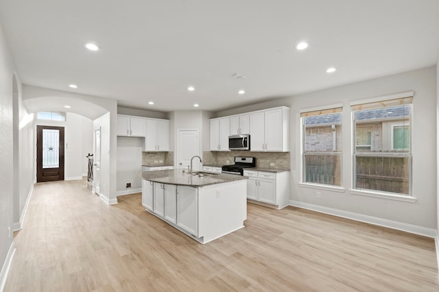 kitchen with stainless steel appliances, a sink, white cabinets, light wood-style flooring, and arched walkways