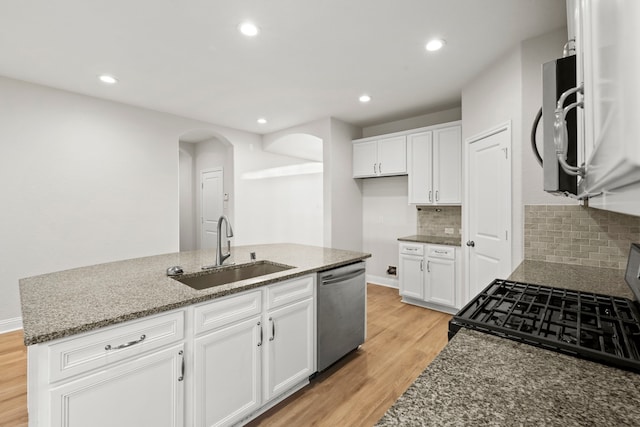kitchen featuring a sink, appliances with stainless steel finishes, arched walkways, light wood-style flooring, and stone countertops