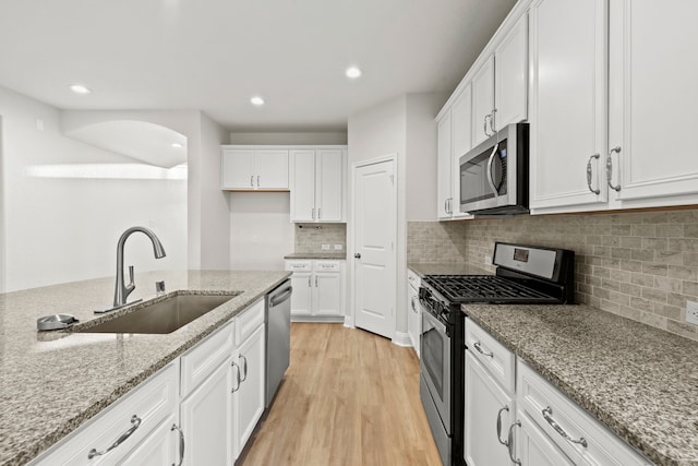 kitchen with appliances with stainless steel finishes, a sink, white cabinetry, light wood-style flooring, and recessed lighting