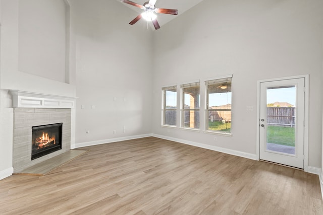 unfurnished living room featuring high vaulted ceiling, a tile fireplace, light wood-type flooring, and plenty of natural light