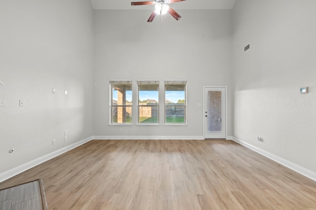 unfurnished living room featuring a towering ceiling, ceiling fan, light wood-style flooring, and baseboards