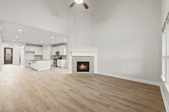 unfurnished living room with a sink, ceiling fan, a fireplace, light wood-type flooring, and recessed lighting