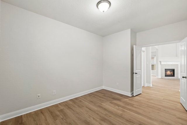 empty room featuring light wood-style flooring, baseboards, and a glass covered fireplace