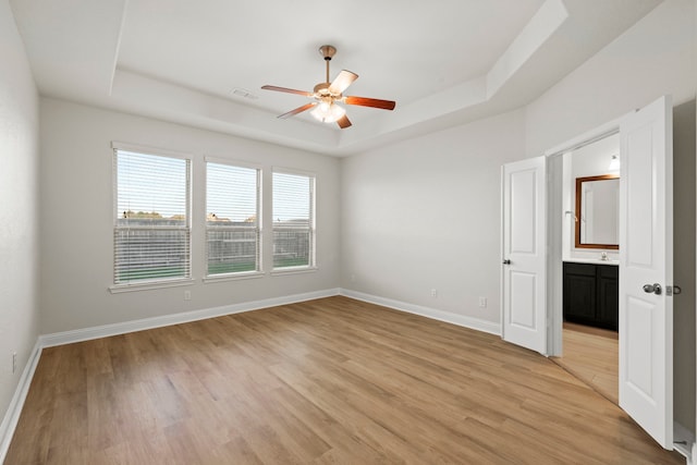 spare room with a tray ceiling, a ceiling fan, light wood-style floors, and baseboards