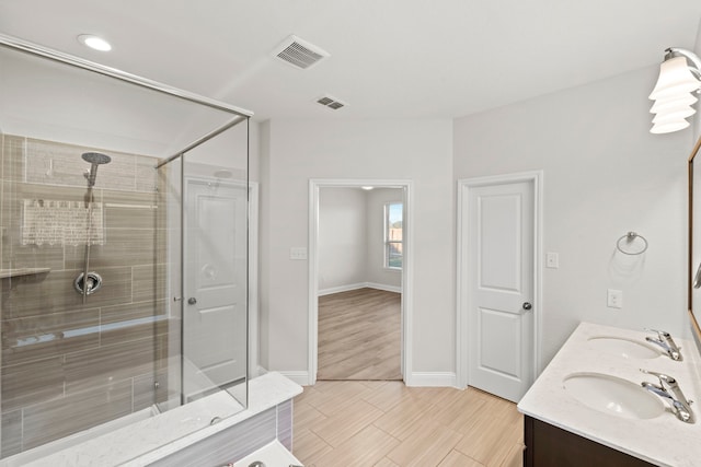 bathroom featuring a stall shower, baseboards, double vanity, and wood finish floors