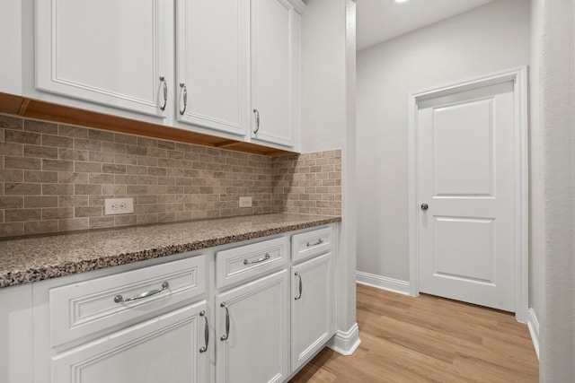 kitchen with light wood finished floors, white cabinetry, tasteful backsplash, baseboards, and stone countertops