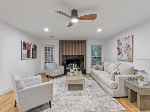 living room with light wood-type flooring, a ceiling fan, recessed lighting, baseboards, and a fireplace