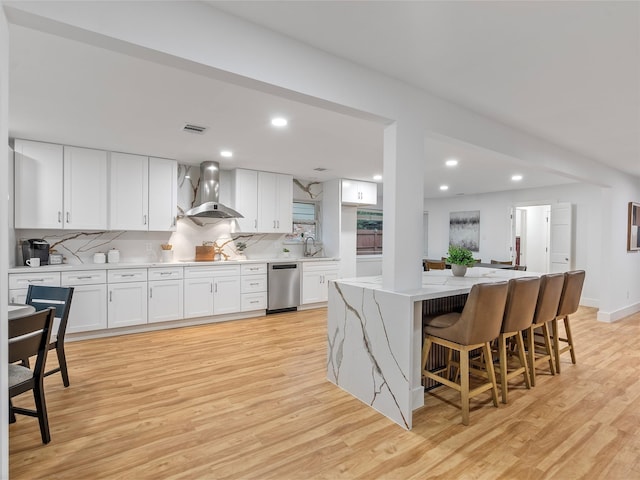 kitchen featuring wall chimney exhaust hood, stainless steel dishwasher, a sink, light wood-style floors, and white cabinets