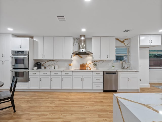 kitchen with stainless steel appliances, wall chimney range hood, a sink, light countertops, and recessed lighting