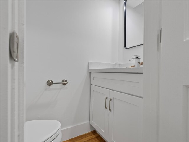 half bath featuring vanity, wood finished floors, toilet, and baseboards
