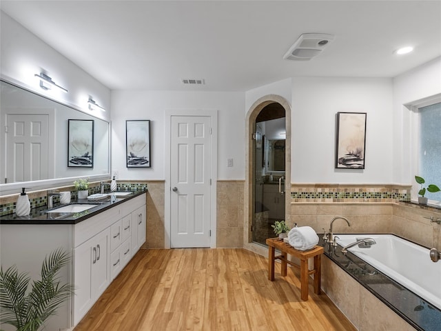 full bathroom with tile walls, wood finished floors, a bath, double vanity, and a shower stall