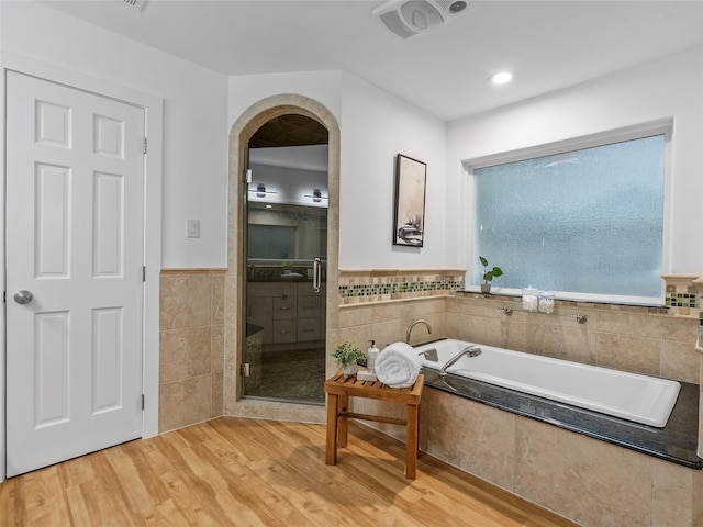 full bathroom with tile walls, a shower stall, wood finished floors, a garden tub, and a wainscoted wall