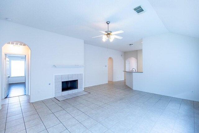 unfurnished living room featuring ceiling fan, arched walkways, a tile fireplace, and lofted ceiling