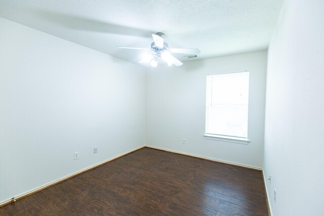 spare room featuring dark wood finished floors, a ceiling fan, and baseboards