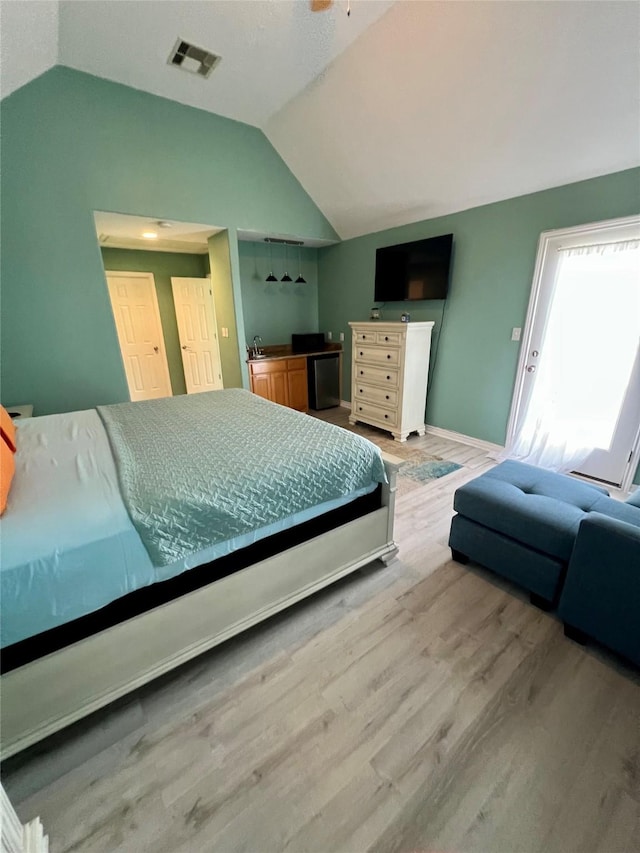 bedroom with lofted ceiling, wood finished floors, a sink, baseboards, and fridge
