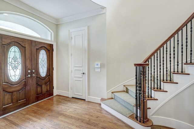 foyer entrance featuring crown molding, wood finished floors, stairs, and baseboards