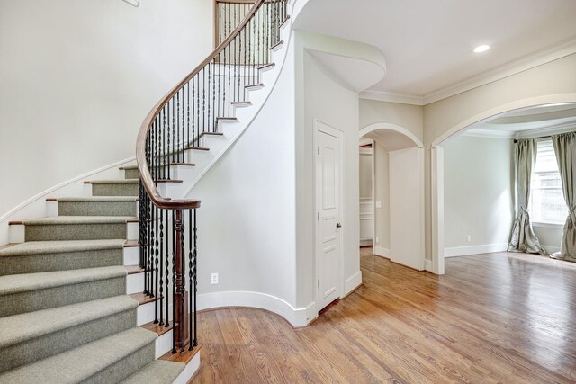 stairs featuring arched walkways, ornamental molding, wood finished floors, baseboards, and recessed lighting