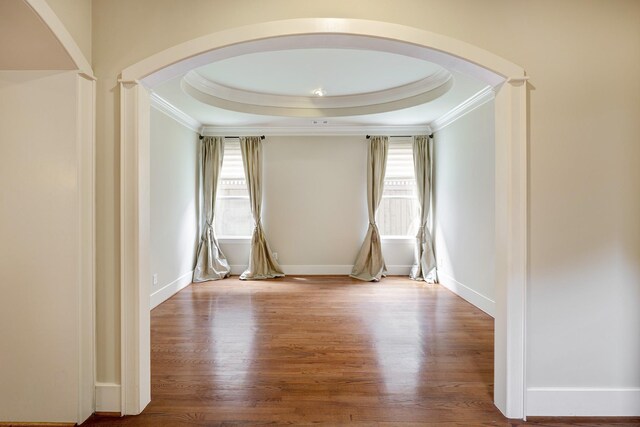 unfurnished room with crown molding, arched walkways, a tray ceiling, wood finished floors, and decorative columns