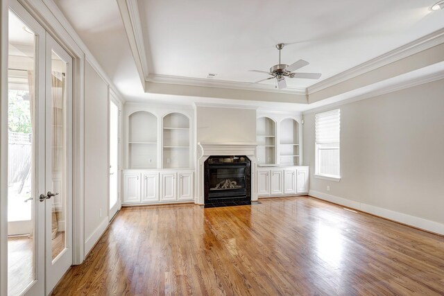 unfurnished living room featuring ornamental molding, a ceiling fan, a premium fireplace, built in features, and light wood-type flooring