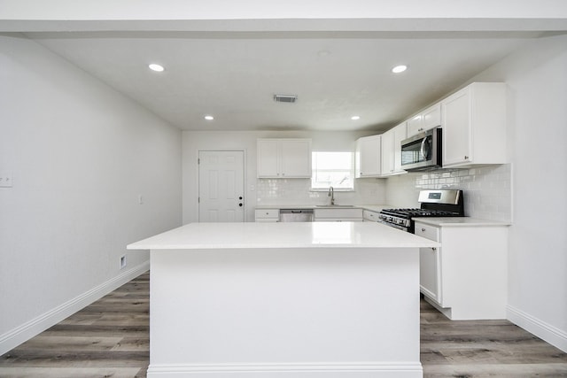 kitchen featuring stainless steel appliances, a sink, a center island, tasteful backsplash, and wood finished floors