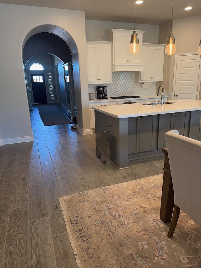 kitchen with a sink, gas stovetop, arched walkways, dark wood-style floors, and white cabinets