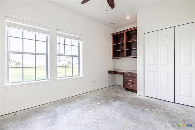 unfurnished bedroom with a closet, concrete flooring, baseboards, and a ceiling fan