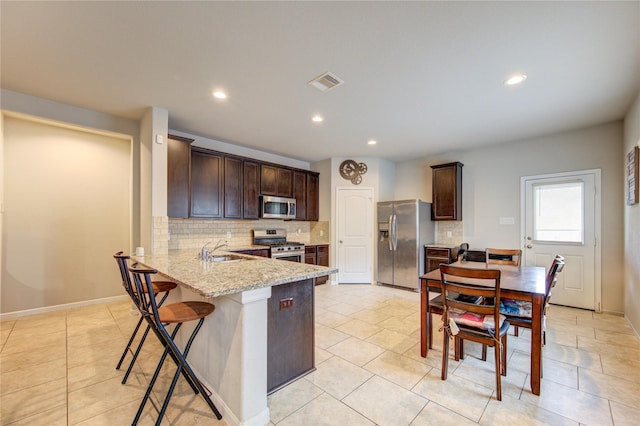 kitchen with appliances with stainless steel finishes, a sink, tasteful backsplash, dark brown cabinets, and recessed lighting